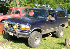1994 Ford Bronco - A blue 1994 Ford Bronco is parked on grass with a red Ford Bronco behind it.