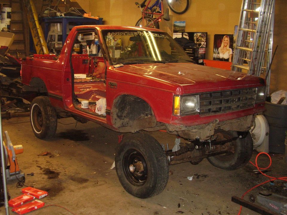 Red two-door pickup in mid-build, door off and front clip stripped, in garage