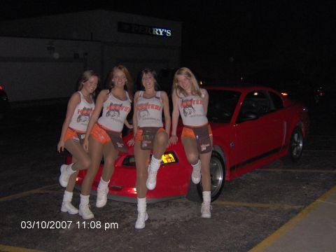 2004 Ford Mustang - Four women in Hooters uniforms pose with a red 2004 Ford Mustang coupe.
