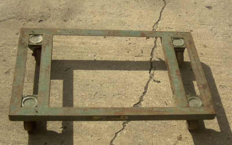 Green metal engine stand with four wheels on concrete