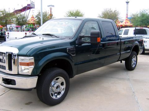 2000 Ford Crown Victoria - A dark green Ford F-250 Super Duty truck is parked in front of a white truck with amusement park rides in the background.