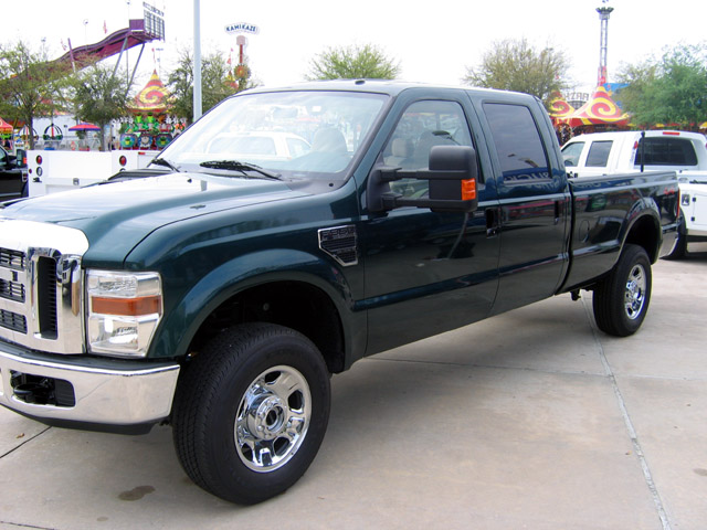 Dark green Ford Super Duty crew cab pickup with chrome wheels parked at a fairground