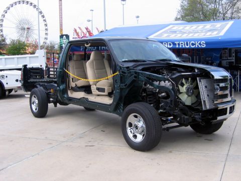 2000 Ford Crown Victoria - A green Ford F-Series truck chassis is displayed outdoors with its front end disassembled, revealing the engine bay components.
