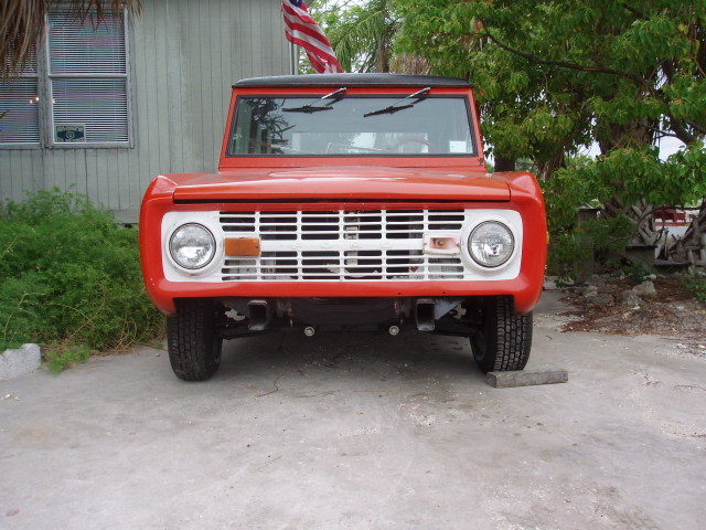 Red 1968 Ford Bronco front view, parked on concrete with an American flag flying behind it
