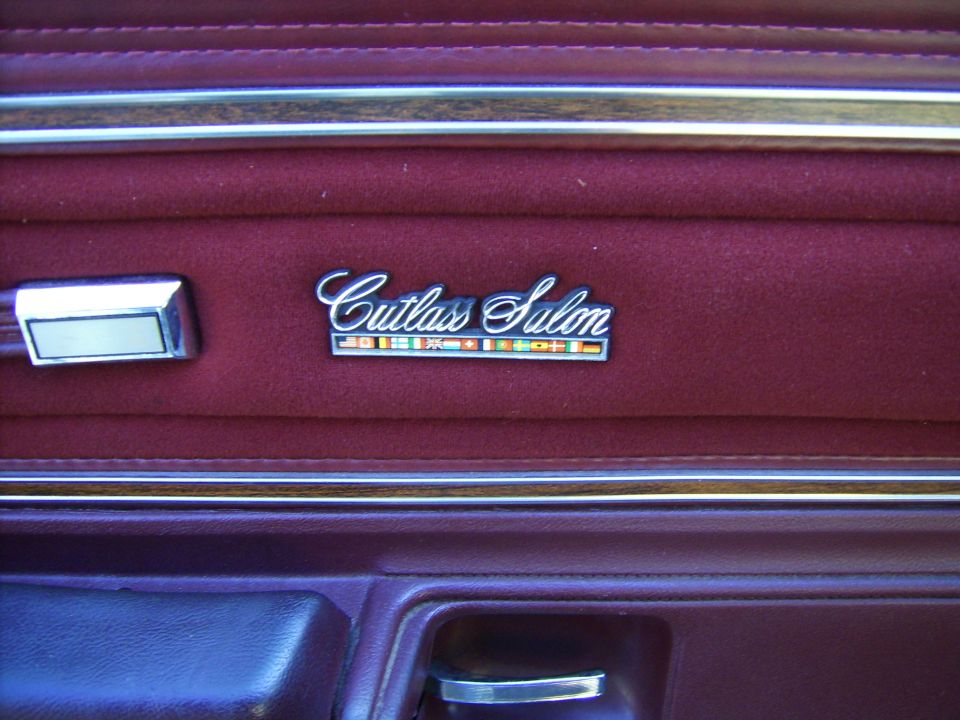 Cutlass Salon emblem with flag row on a burgundy door panel