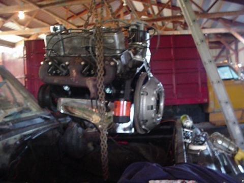 1992 Ford Bronco - A used V8 engine hangs from a hoist chain inside a wooden barn, shown from the driver's side with an exposed clutch and pressure plate on t…