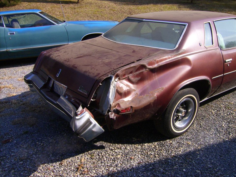 Burgundy Oldsmobile Cutlass coupe with crushed rear quarter panel on gravel lot