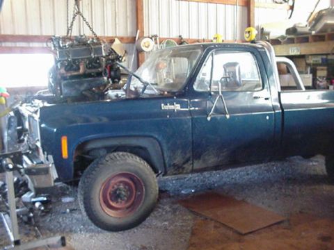1992 Ford Bronco - A blue pickup truck is undergoing an engine replacement, with the new engine being lowered into place.