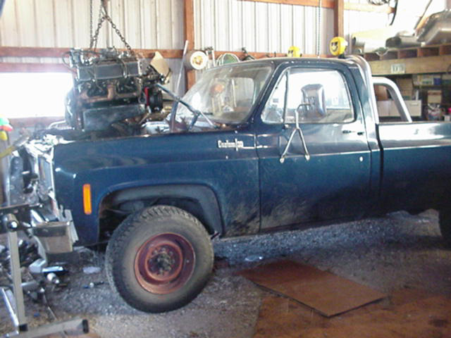 Blue pickup truck, possibly 1973 Chevrolet C/K, with engine suspended by chains above the engine bay