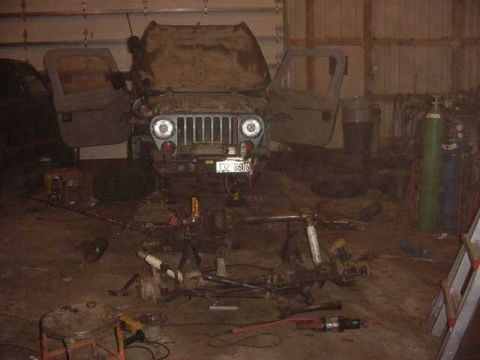 1992 Ford Bronco - This Jeep CJ-5 is in a garage with its hood and doors open, surrounded by various automotive parts and tools.