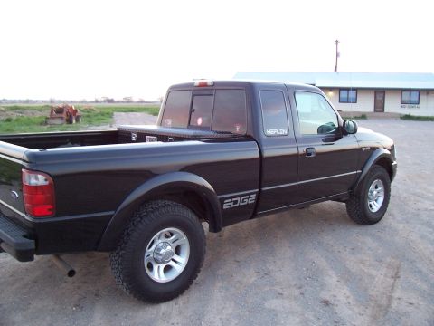 2003 Ford Ranger - A black 2003 Ford Ranger pickup truck is parked on a gravel lot in front of a building.