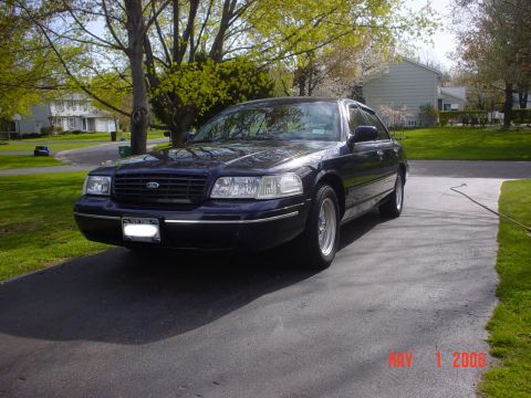 2000 Ford Crown Victoria - A dark blue Ford Crown Victoria is parked in a suburban driveway on a sunny day.