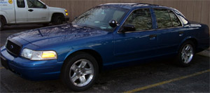 2000 Ford Crown Victoria - A blue 2000 Ford Crown Victoria is parked next to a white truck.