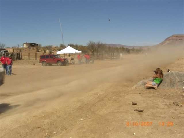 Dust cloud rising from a dirt road as a girl photographs near a ranch and tent