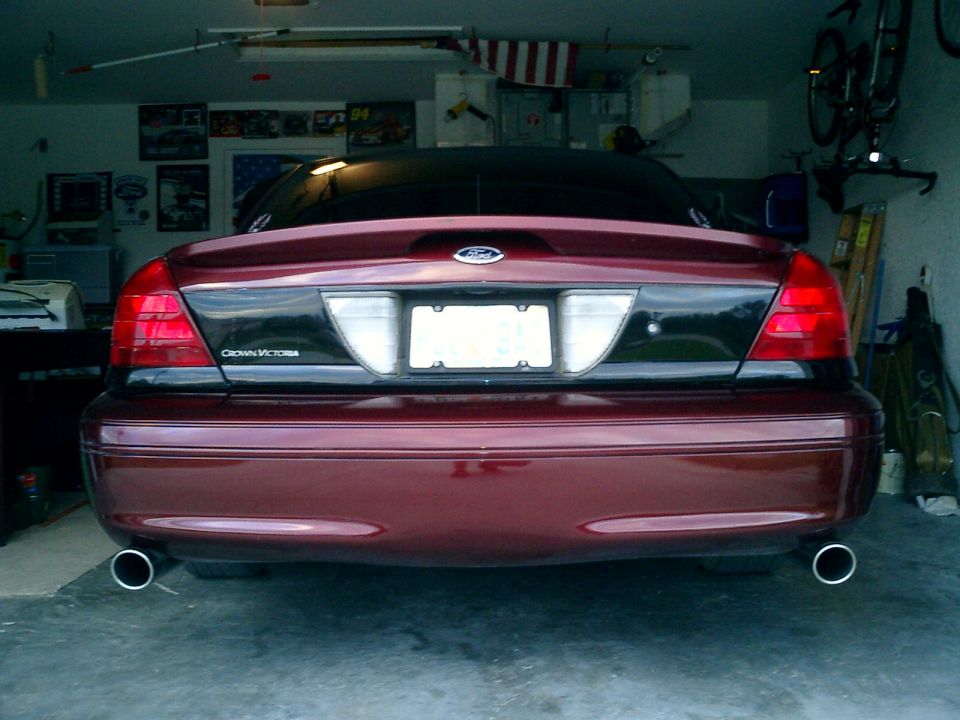 Rear view of a dark red Ford Crown Victoria with dual chrome exhaust tips in a home garage