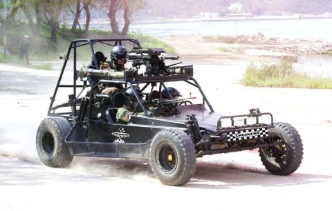1968 Ford Mustang - A military buggy with multiple weapons systems and armed personnel drives on a dirt road, kicking up dust.