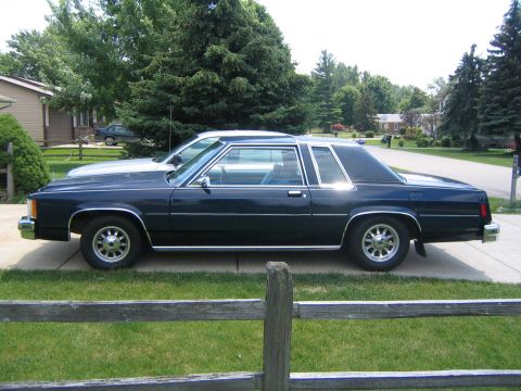 1999 Mercury Grand Marquis - This car is parked in a suburban driveway with a fence in the foreground and trees in the background.