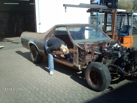 1979 Ford Ranchero - A person works on the interior of a heavily rusted pickup truck, with a forklift visible in the background.