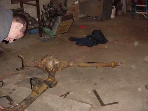 1992 Ford Bronco - A rusty rear axle assembly sits on a concrete floor in what appears to be a garage or workshop.