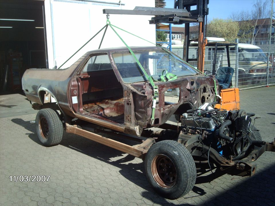 Brown 1979 Ford Ranchero body being lifted by a forklift, engine exposed, doors removed