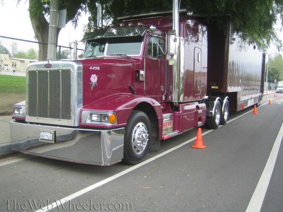 Maroon Peterbilt semi-truck with chrome grille and bumper, parked on the side of the road with orange cones