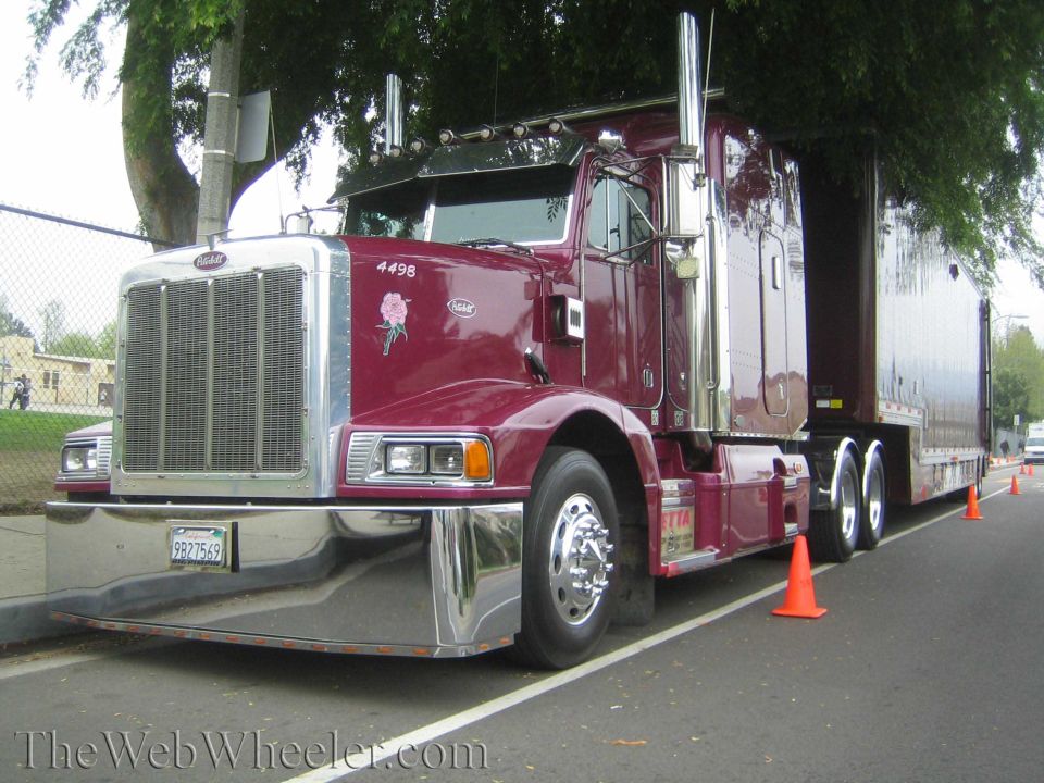 Maroon Peterbilt semi-truck with chrome grille and bumper, parked on asphalt
