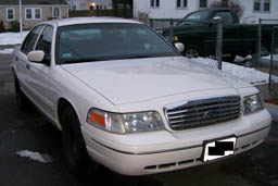 1999 Ford Crown Victoria - Front view of a white sedan with a chrome grille, parked in a residential area.