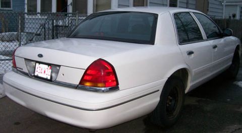 1999 Ford Crown Victoria - A white 1998 Ford Crown Victoria is seen from the rear 3/4 angle, with visible damage on the rear bumper and driver's side rear door.