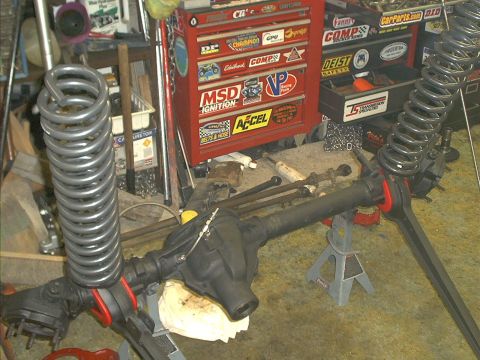 1986 Ford Bronco - A garage scene shows a front axle assembly and coil springs, with toolboxes in the background.