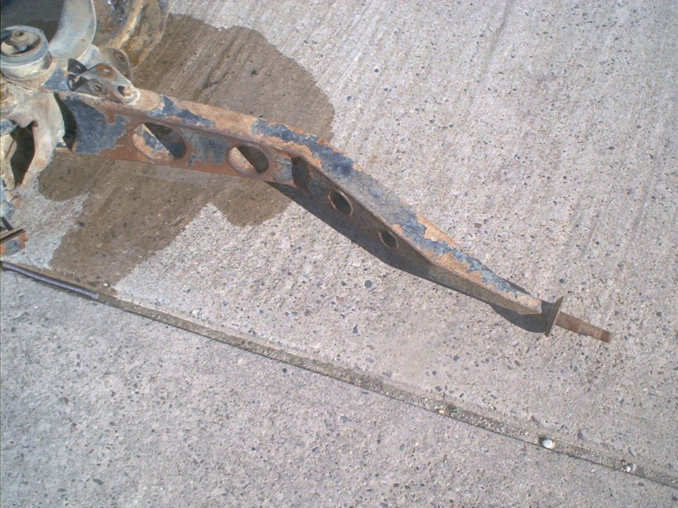 Rusty suspension arm with circular cutouts on concrete
