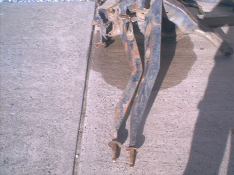 1986 Ford Bronco - Close-up view of heavily rusted vehicle frame components resting on a concrete surface.