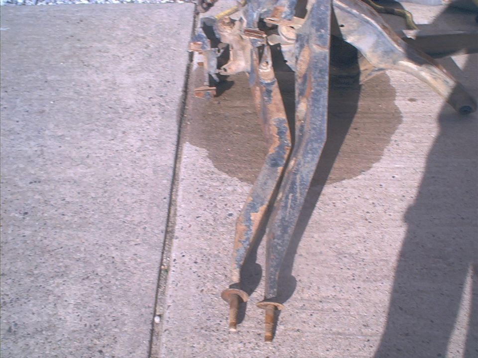 Rusted metal frame components on concrete, showing bolts and structural elements