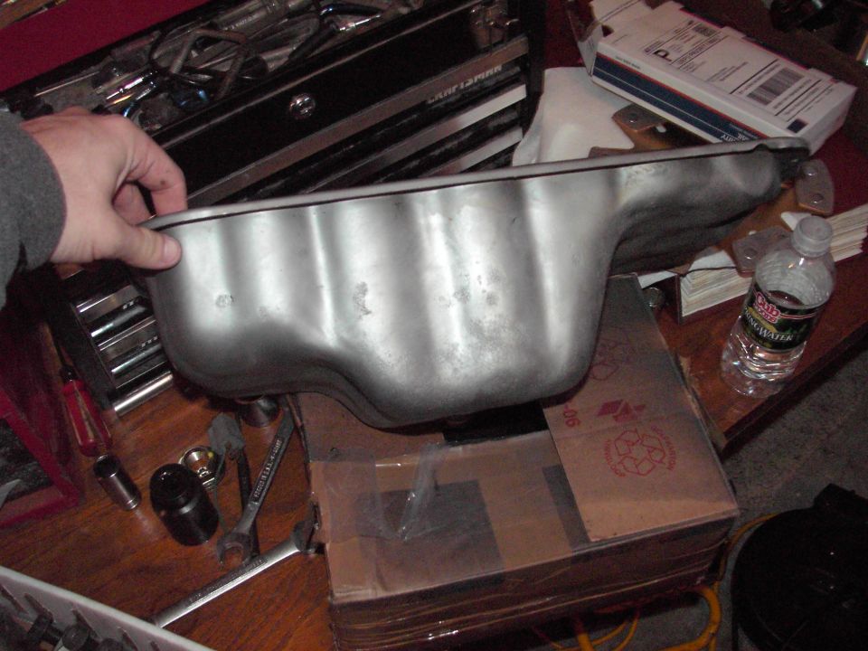Metal oil pan held by a hand over a toolbox and boxes