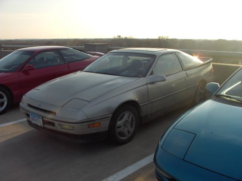 1989 Ford Probe - A silver 1989 Ford Probe is parked in a lot with other vehicles, its distinctive pop-up headlights visible.