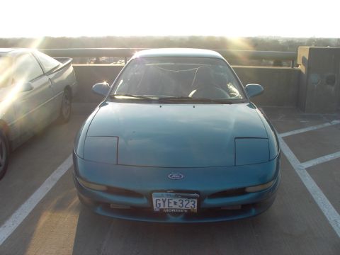 1989 Ford Probe - Two cars are parked on a rooftop or parking garage level with the sun setting in the background.