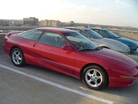 1989 Ford Probe - A red coupe is parked in a lot with two other vehicles visible behind it.