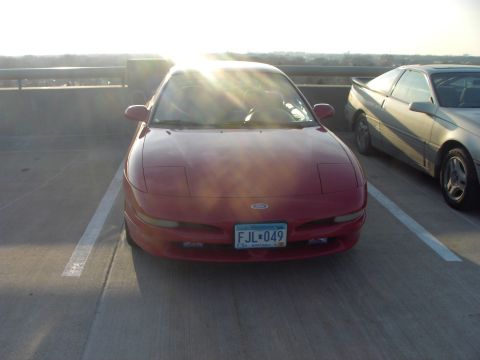 1989 Ford Probe - Two Ford Probes are parked in a lot, one red and one silver, with the sun glinting off the windshield of the red car.