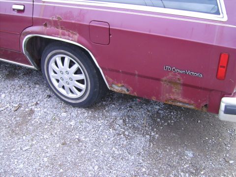 1982 Ford LTD Crown Victoria - This maroon station wagon shows significant rust damage on its rear quarter panel and lower body.