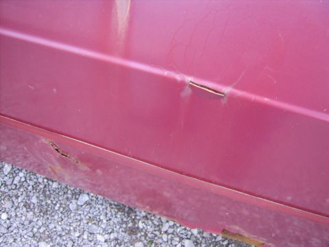 1982 Ford LTD Crown Victoria - Close-up of damaged maroon/burgundy body panel showing a dent and split seam along the body crease, spider-web paint cracking above it, and…
