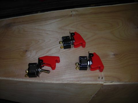 1994 Ford Bronco - Three toggle switches with red covers are shown on a wooden surface, possibly for automotive use.