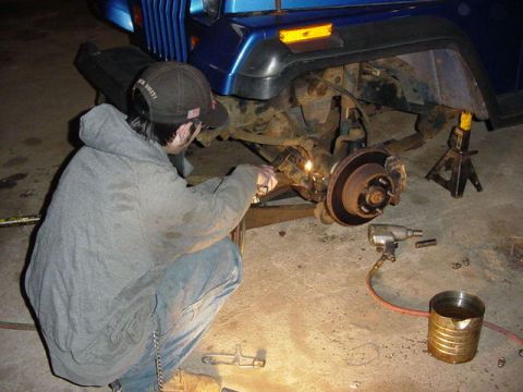 1992 Ford Bronco - A person is welding on the suspension of a blue vehicle that is raised on jack stands.
