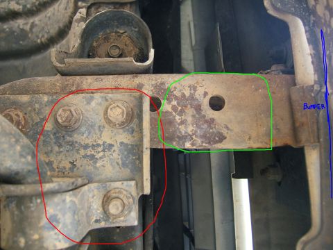 1991 Ford Bronco - Close-up of a rusted frame bracket and bumper mount, showing bolts and surface corrosion.