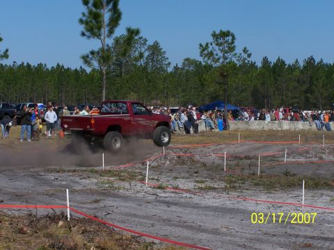1989 Ford Bronco - Red pickup truck navigates an off-road course with spectators in the background.
