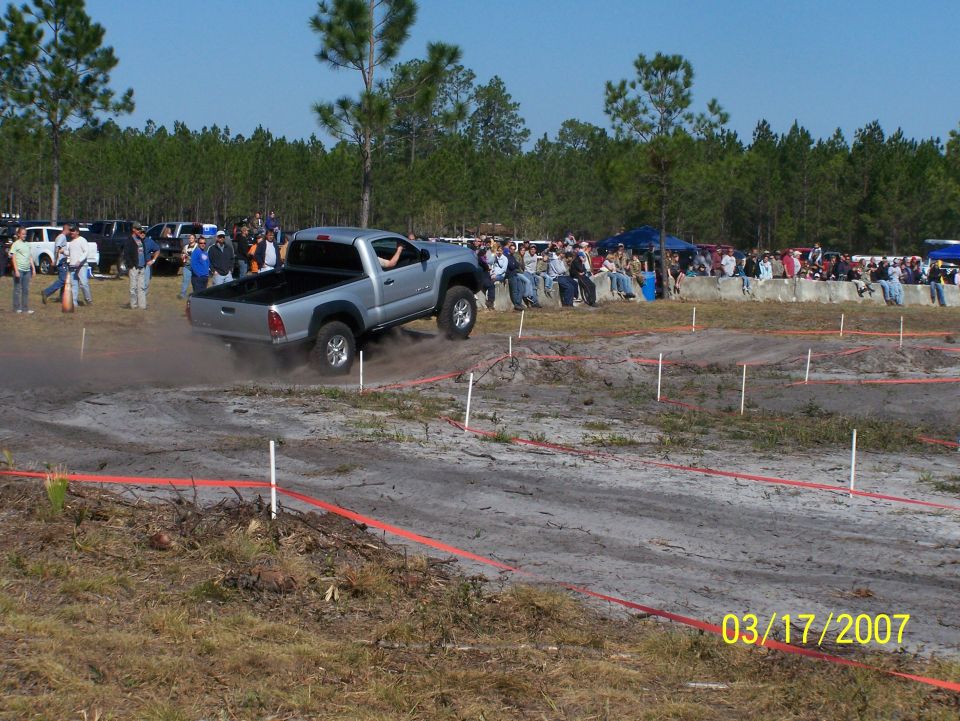 Silver pickup truck kicking up dust on a dirt track, spectators in background