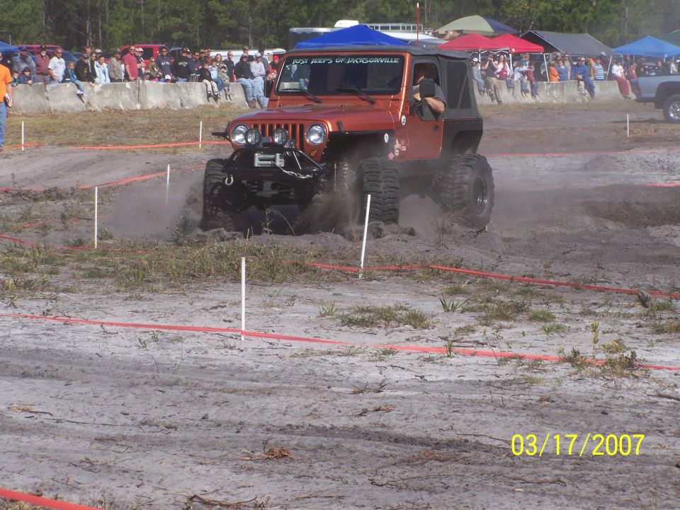 Orange Jeep Wrangler driving through mud with spectators in background. Date stamp 03/17/2007