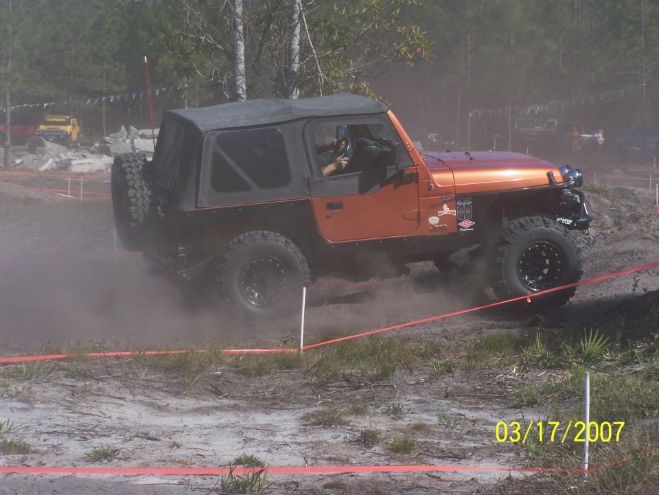 orange Jeep Wrangler kicking up dust on a dirt track