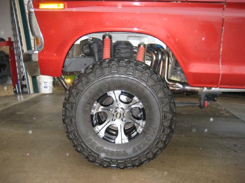 1979 Ford Bronco - Close-up of a red pickup truck's front wheel, suspension, and fender, showing aftermarket modifications.
