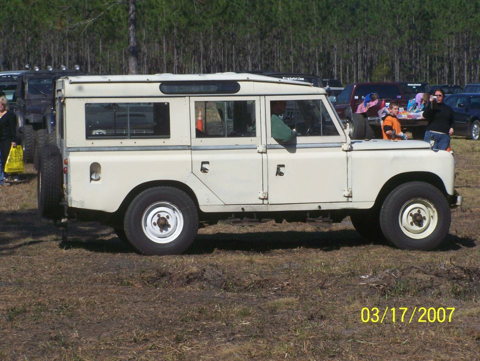 Cream-colored Land Rover Series III station wagon, side view, with spare tire on rear. Appears to be in fair condition