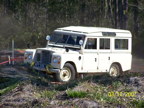 1989 Ford Bronco - A white Land Rover Defender navigates a rough terrain course on a sunny day.