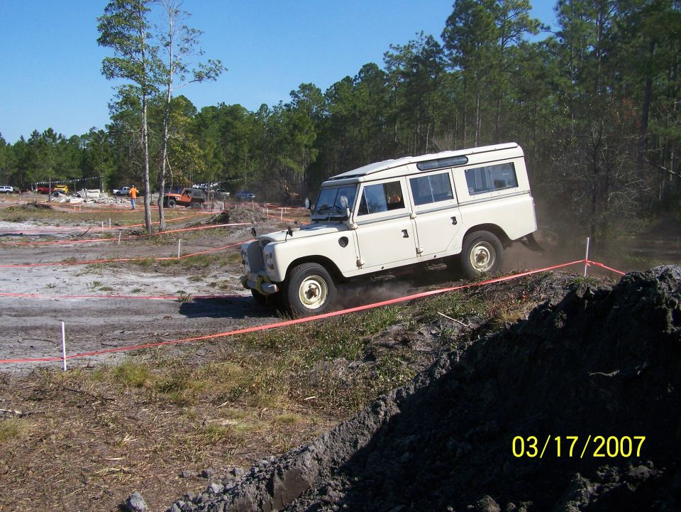White Land Rover Defender 110 on muddy off-road course